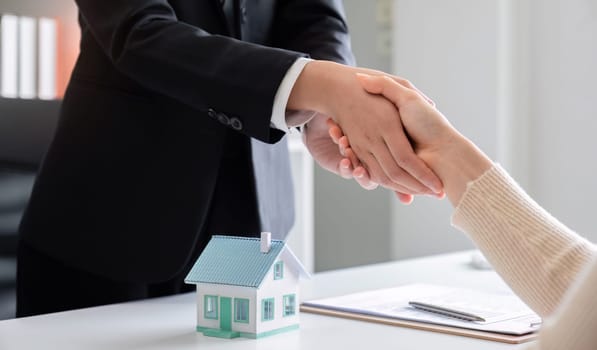 Real estate agent or realtor shakes hands with her client after making the deal in the office.