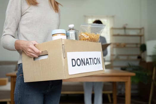 Beautiful female volunteer holds a donation box with canned food in it..