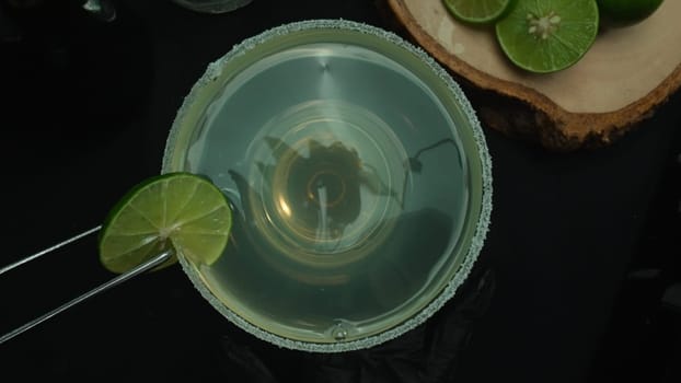 Macrography, a top-down view of a refreshing margarita is presented in a glass adorned with a green lime slice, all set with black background. Each close-up shot of the cocktail and lime. Comestible.