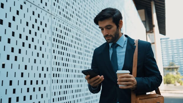 Smart manager looking at mobile phone and walking at street while wearing suit. Skilled investor looking mobile phone to checking sales or working while holding coffee cup. White background. Exultant.