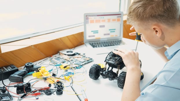 Top view of happy student study car model construction at table with electronic equipment and laptop display coding program screen scatter around at STEM classroom. Creative education. Edification.