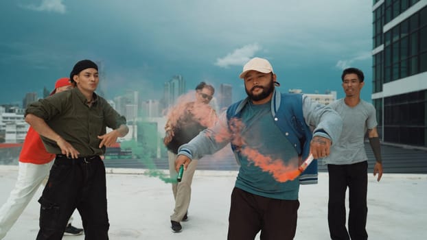 Group of multicultural hipster playing color flare at rooftop. Attractive street dancer holding colored smoke and perform break dance move to hip-hop music. Outdoor sport 2024. Endeavor.