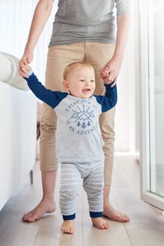 Parent, boy and baby in home, walking and learning with support, growth and development of child. House, happy and cute toddler with smile, wood and floor in apartment, steps and standing with care.