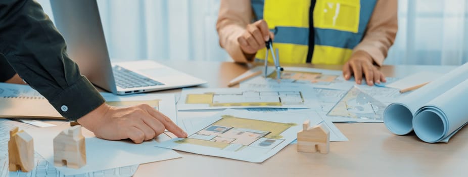 Skilled engineer uses divider to measure the blueprint while architect pointing the mistake point in the building blueprint on table with architectural document scatter around. Close up. Delineation.