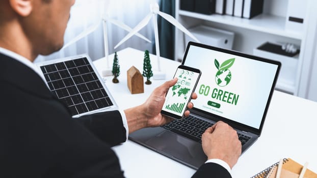 Businessman working in office developing plan or project on eco-friendly alternative energy with solar cell technology display on computer screen for greener environment as apart of CSR effort. Gyre