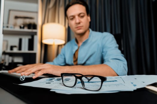 Smart businessman typing with keyboard on monitor with business paragraph dynamic data marketing analysis planning sheet aligning on report paperwork at modern home office at night time. Pecuniary.