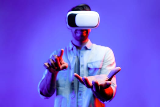 Caucasian smart man with VR glasses while holding hologram display in VR. Happy person holding and pointing while looking by using goggle and headset with neon light background. Technology. Deviation.