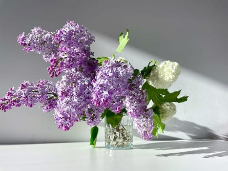 A bouquet of blossoming purple lilac flowers and a white viburnum inflorescence on a gray background. High quality photo