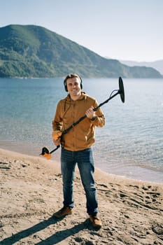 Smiling beach cop with a metal detector stands on the seashore. High quality photo