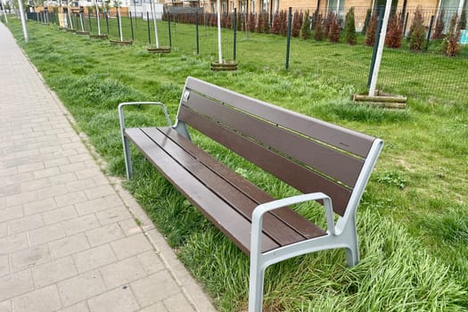 In the city, there is a bench for rest on the side of the pedestrian sidewalk. High quality photo