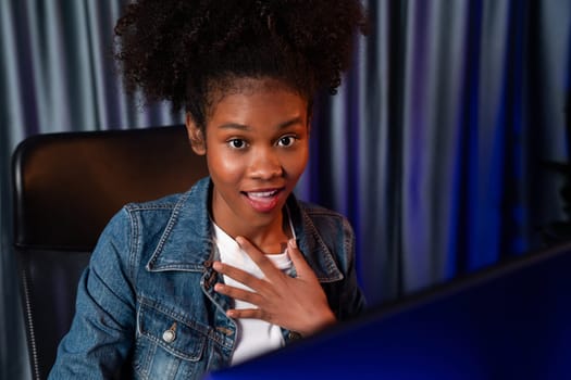 Young African American woman with surprise face, wearing blue jeans shirt and looking at final project document on laptop for planing next sequence. Concept of work at neat home place. Tastemaker.