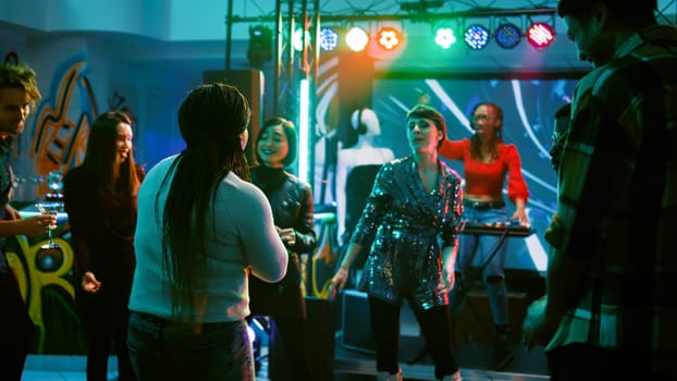 Persons having fun at dance party, partying together on electronic music at discotheque. Cheerful group of friends enjoying night out at club, dancing around for entertainment. Handheld shot.