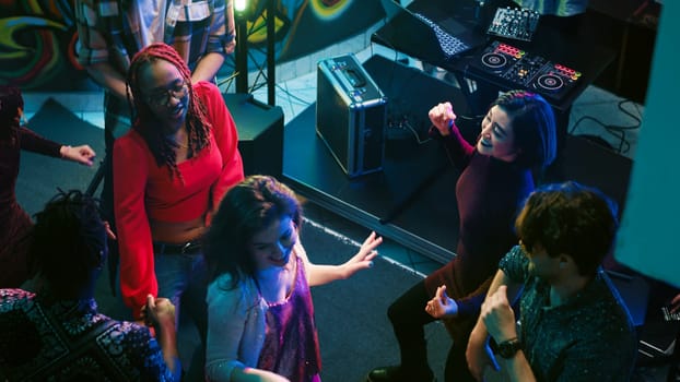 Cheerful persons doing dance moves at club, partying together on the dance floor. Modern crowd of people listening to music and dancing, having fun at nightclub for entertainment. Handheld shot.