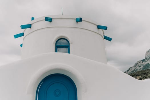 A blue door is on a white building. The building is small and has a blue roof. The sky is cloudy and the building is on a hill