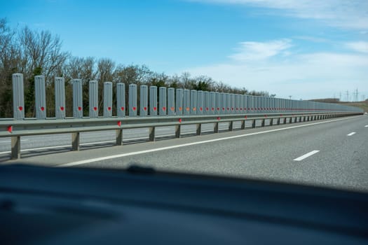 A road with a long line of metal posts with red hearts on them. The road is empty and the sky is clear