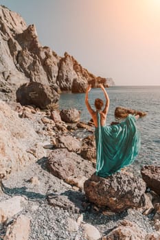 Woman green dress sea. Woman in a long mint dress posing on a beach with rocks on sunny day. Girl on the nature on blue sky background