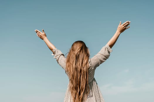 A woman with long hair is standing on the beach, looking up at the sky. She is wearing a dress and she is happy