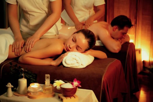 Caucasian couple customer enjoying relaxing anti-stress spa massage and pampering with beauty skin recreation leisure in warm candle lighting ambient salon spa at luxury resort or hotel. Quiescent