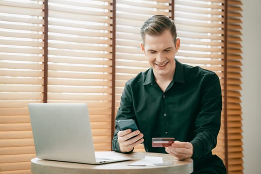 Young man using laptop with credit card for internet banking, online shopping E commerce by online payment gateway at home office. Modern and convenience online purchasing with debit card. Unveiling
