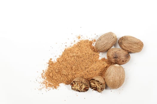 Spoon of ground nutmeg, whole and halved seeds over white background. Muscat nuts closeup for spice and seasoning concept. Myristica fragrans tree organic fruits for herbal medicine.