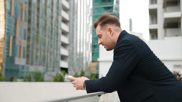 Professional businessman using phone to chatting with team while standing roof top. Happy smart project manager working on telephone with skyscraper view while communicate with marketing team. Urbane.