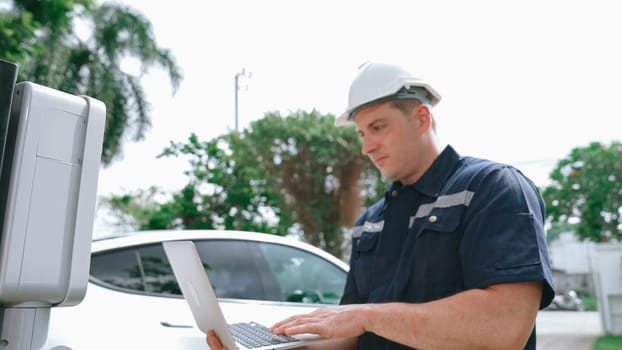 Qualified technician working on home EV charging station installation, making troubleshooting and configuration setup on charging system with laptop for EV at home. Synchronos