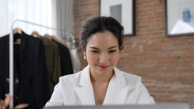 Young businesswoman sitting on the workspace desk using laptop computer for internet online content writing or remote working from home. Clothing and textile business marketing analysis. Vivancy