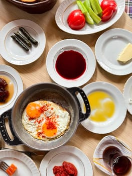 Traditional Turkish breakfast with scrambled eggs in frying pan, sliced tomatoes and cucumbers, variety of jams, honey, butter, rolled grape leaves, top view. Healthy eating concept. High quality