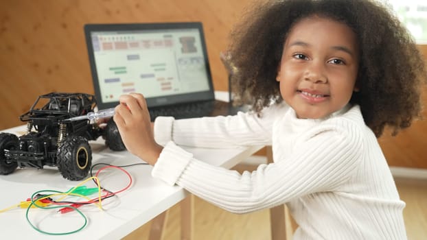 Smart african girl build robotic car while using wires while using laptop setting or writing prompt code. Skilled female student working on computer in STEM technology online classroom. Erudition.