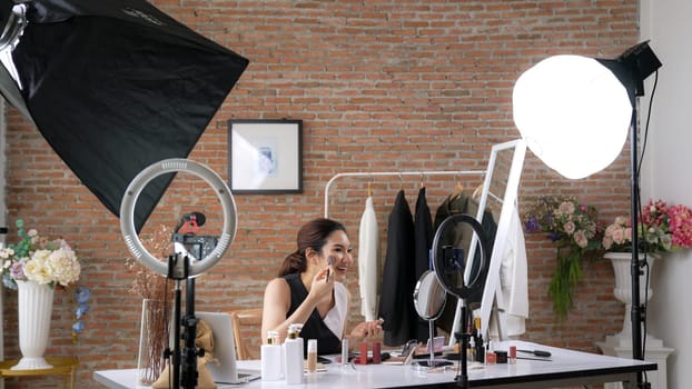 Woman influencer shoot live streaming vlog video review vivancy makeup social media or blog. Happy young girl with cosmetics studio lighting for marketing recording session broadcasting online.