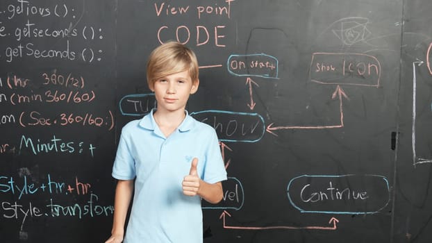 Smart caucasian boy standing at blackboard with engineering prompt or system code and showing a thumb. Student planing a project by using coding and programing system in STEM classroom. Erudition.