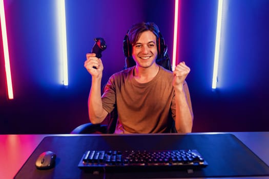 Enjoy smart gaming streamer with control joystick, playing game online of live streaming social media group with team skilled players on computer at modern technology cyber neon light room. Pecuniary.