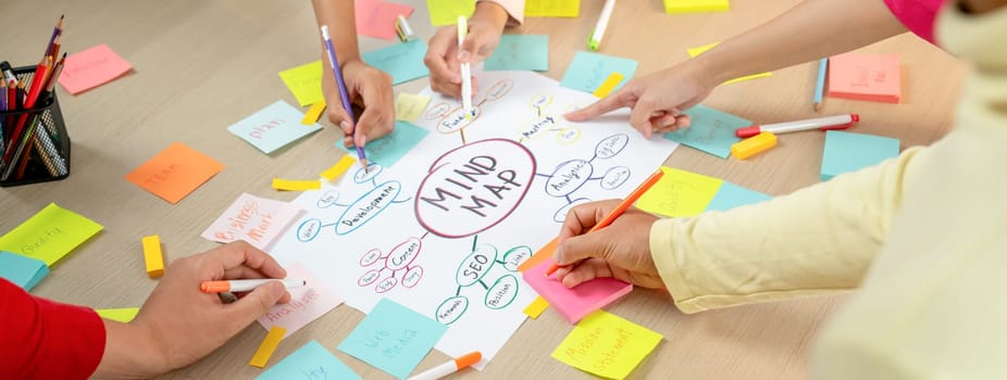 Professional startup group share creative marketing idea by using mind map. Young skilled business people brainstorm business plan while writing sticky notes. Focus on hand. Closeup. Variegated.