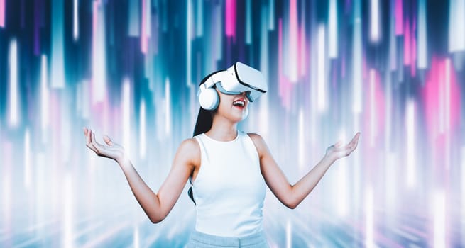 Female standing and wearing white VR headset and white sleeveless connect metaverse, future technology creating cyberspace community. She enjoy look fantasy abstract light around her. Hallucination.