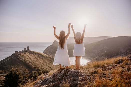 Two women are standing on a hill overlooking the ocean. They are holding hands and looking out at the water. The scene is peaceful and serene, with the sun shining brightly in the background