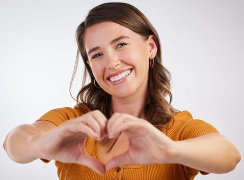 Happy woman, portrait and heart hands with love in care, romance or kindness on a gray studio background. Young female person with smile for shape, like emoji or support for review, gesture or symbol.