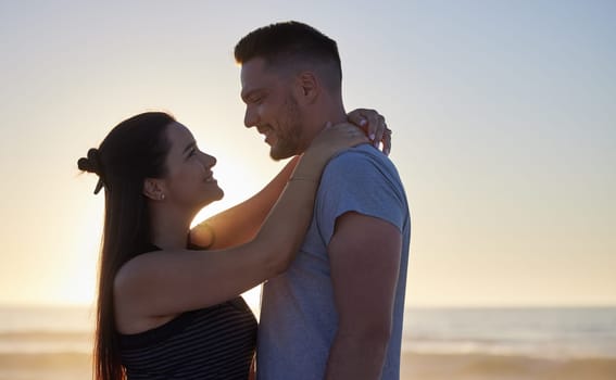 Couple, hug and sunset for holiday on beach with smile, love and romance for anniversary or honeymoon. People, happy and embrace by ocean for summer sunrise, morning date and healthy relationship.