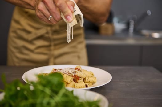 Close-up chef's hands seasoning and decorating meal with grated parmesan cheese and arugula leaves, cooking pasta with tomato sauce according to traditional Italian recipe. Cuisine. Culinary. Epicure