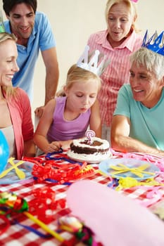 Portrait, candle or girl at family, birthday or party to wish, support or love by bonding together. Papa, child or granny to blow, cake or paper hats in home for memory of childhood growth milestone.