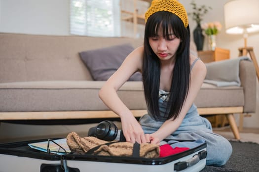 A woman is sitting on the floor of her home, sorting through her luggage. She is wearing a yellow hat and she is in a bad mood