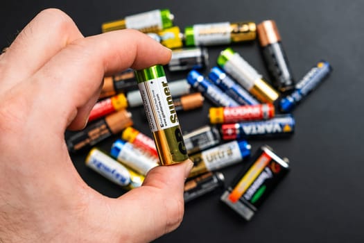 BERLIN , GERMANY - APRIL 14 2024: Used alkaline AA batteries in mans hand and on the black table.