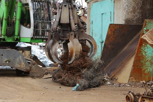 A green-colored crane loads scrap metal for recycling, at a raw material recycling facility.