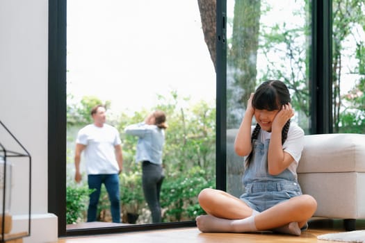 Stressed and unhappy girl huddle in corner, cover her ears with painful expression while her parent arguing in background. Domestic violence and traumatic childhood develop to depression. Synchronos