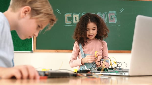 Girl standing while fixing electronic board by using screwdriver. American student and happy caucasian boy working together to inspect electric system. Curious children working on board. Pedagogy.