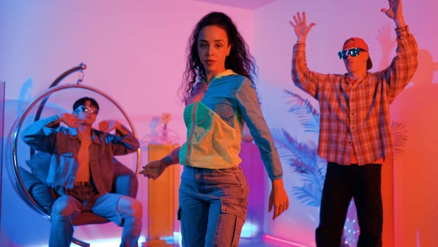 Attractive happy dancer looking at camera while smart woman moving at rhyme with neon light. Professional hispanic performer break dancing while wearing colorful cloth with diverse friend. Regalement.