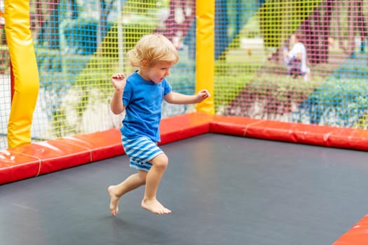 Toddler boy in blue outfit jumping on colorful outdoor trampoline. Playful activity and fun concept. Design for banner, poster.