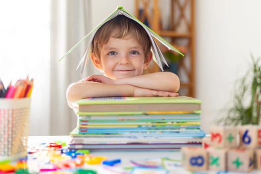 Cheerful boy with stack of books under paper roof. Joyful learning concept. Creative education and imagination theme. Design for educational poster, invitation to reading event, book club flyer.