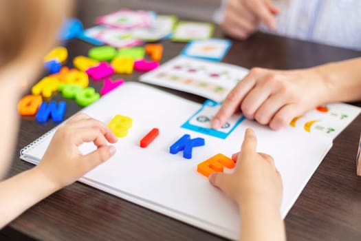 Child and adult hands arranging colorful plastic letters on a white background. Early education and literacy concept for design and print.