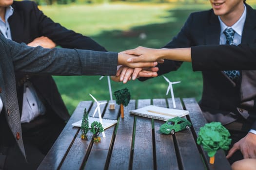 Business people join hand together as teamwork and unity, outdoor business meeting table. Eco-friendly practices and collaboration in corporate social responsibility for greener environment. Gyre