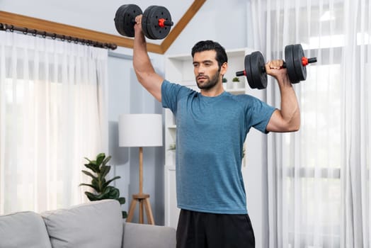 Athletic body and active sporty man lifting dumbbell weight for effective targeting muscle gain at gaiety home as concept of healthy fit body home workout lifestyle.